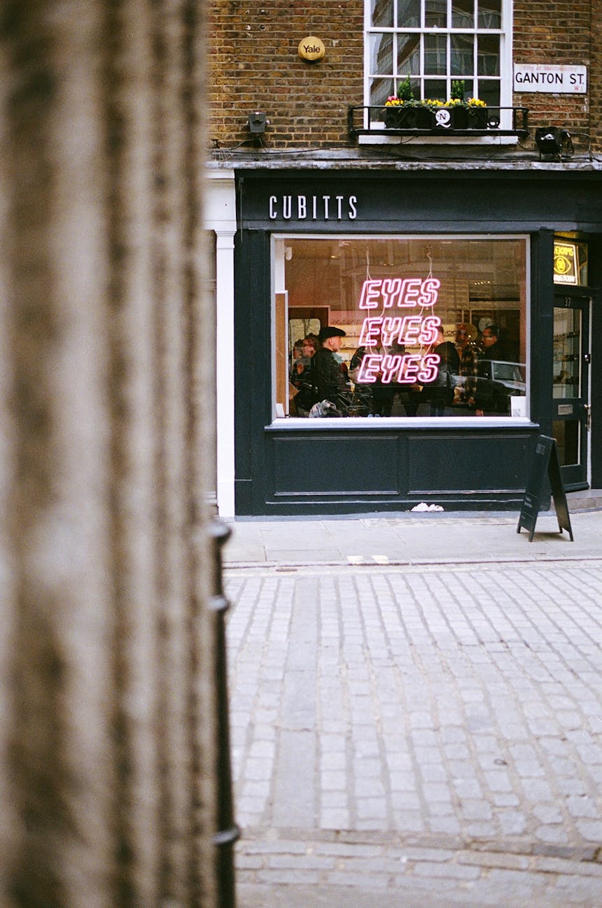 Facade of an urban optician shop with a neon sign on a cobblestone street.