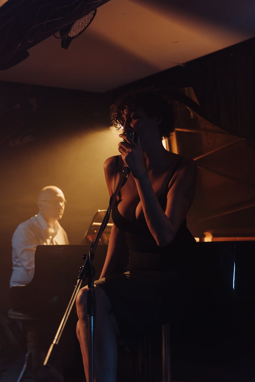 A jazz singer and pianist perform under warm lighting in a cozy indoor setting, capturing the essence of live music.
