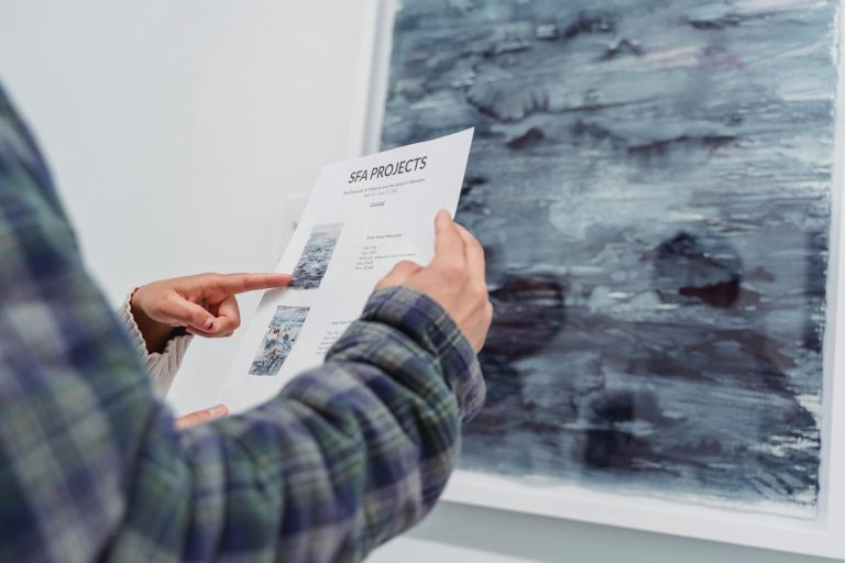 Close-up of a person examining an art gallery project document in front of artwork.
