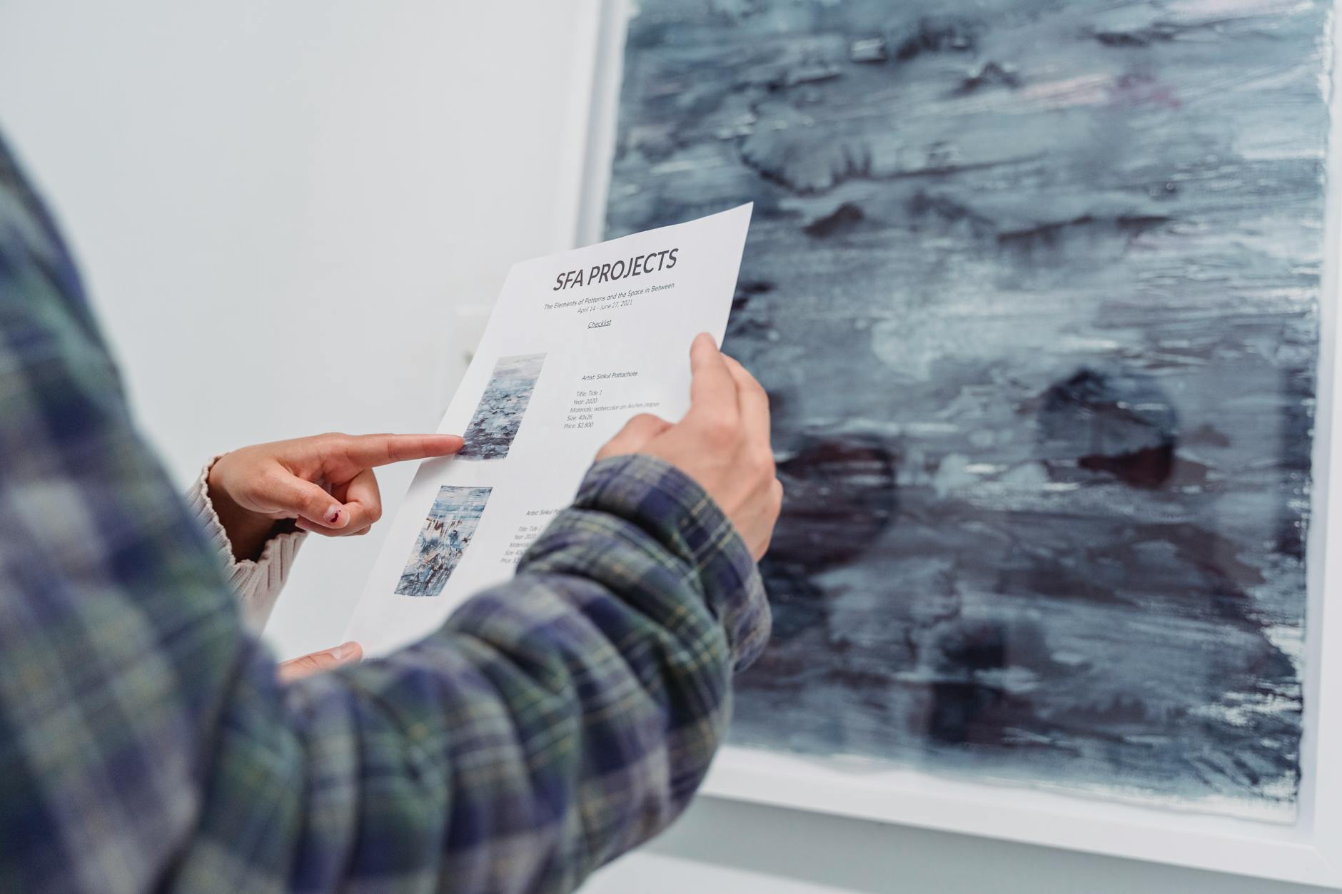 Close-up of a person examining an art gallery project document in front of artwork.