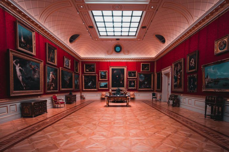 Explore the grandeur of an art gallery room in London with elegant red walls and classic paintings.