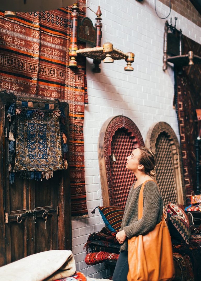 A woman admires traditional rugs and textiles in a vibrant indoor market setting.