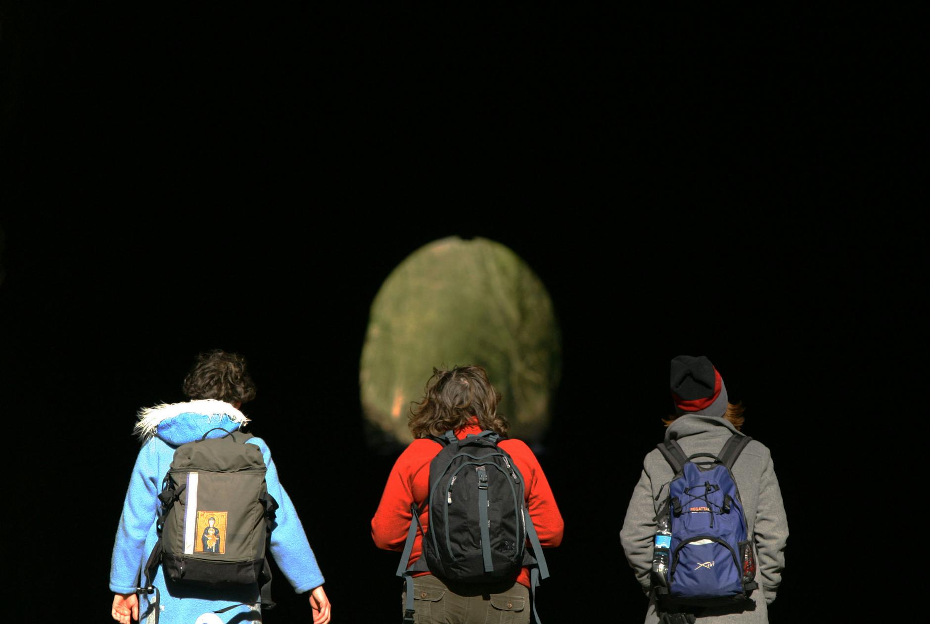 Three friends backpacking through a dark tunnel towards daylight in Bristol, UK.