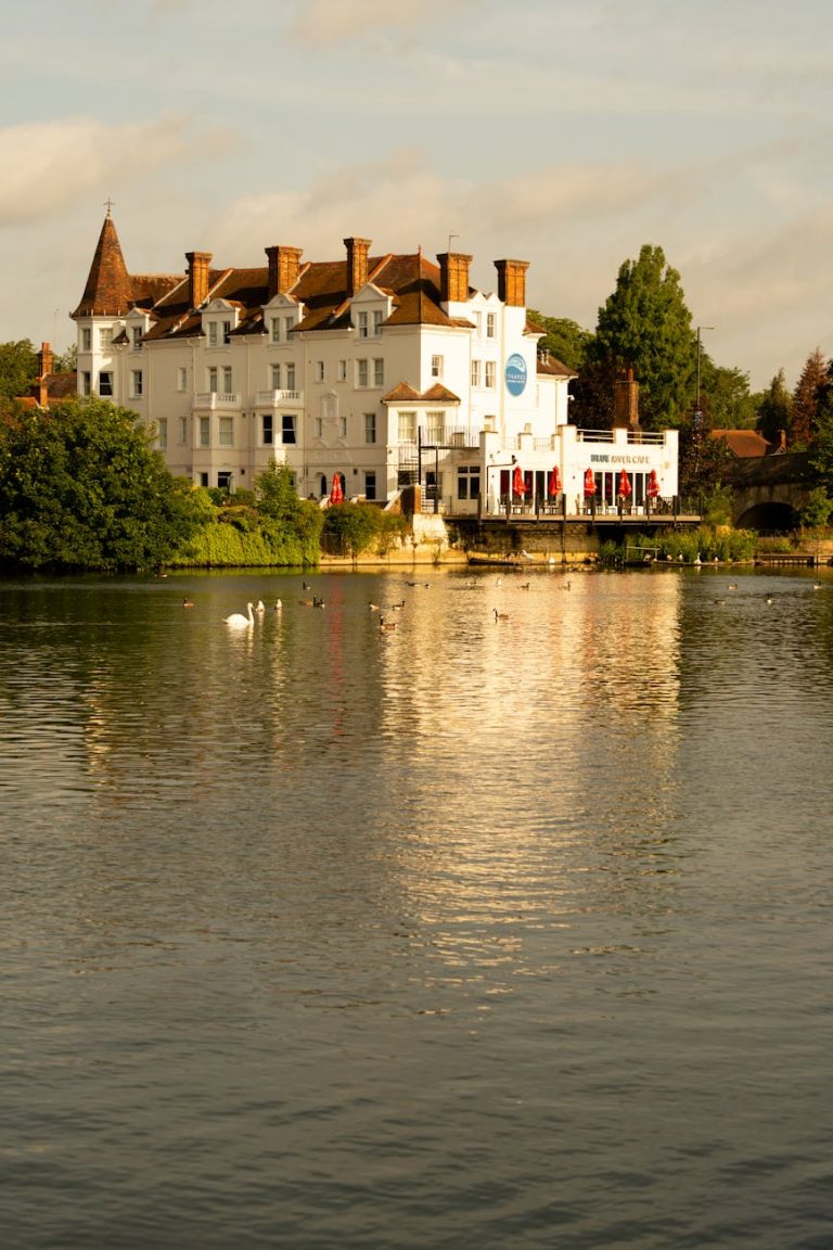 Picturesque white building by the river with swans reflecting summer sunset light, perfect for leisure and UK travel.