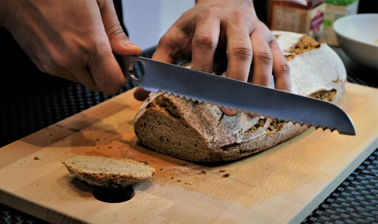 Person slicing artisan bread on a wooden cutting board with a serrated knife.
