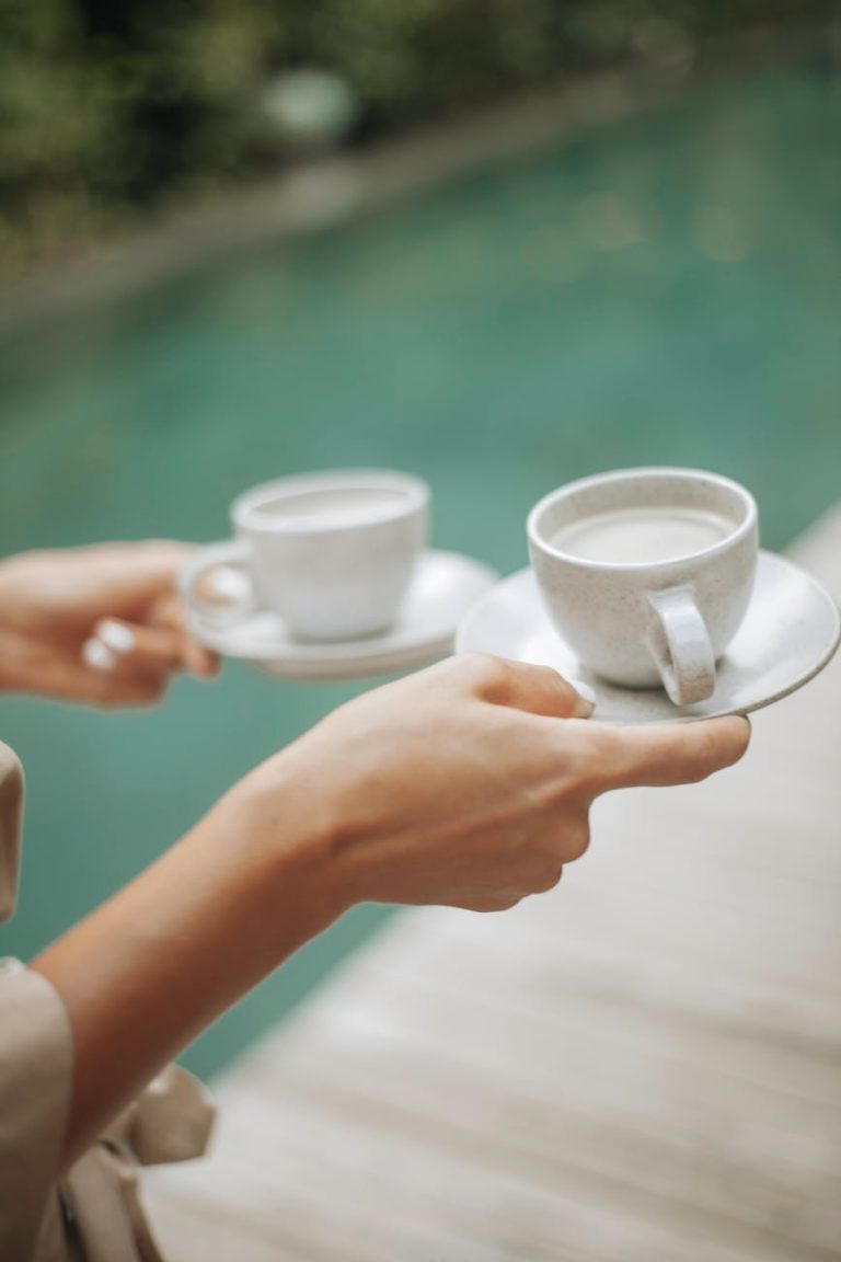 Hands holding coffee cups by a poolside, perfect for a leisure morning.