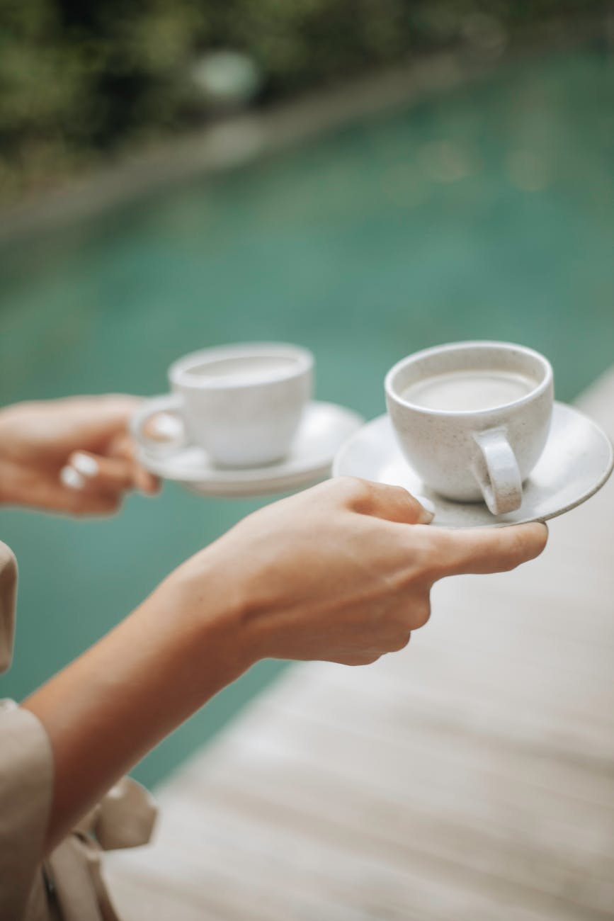 Hands holding coffee cups by a poolside, perfect for a leisure morning.