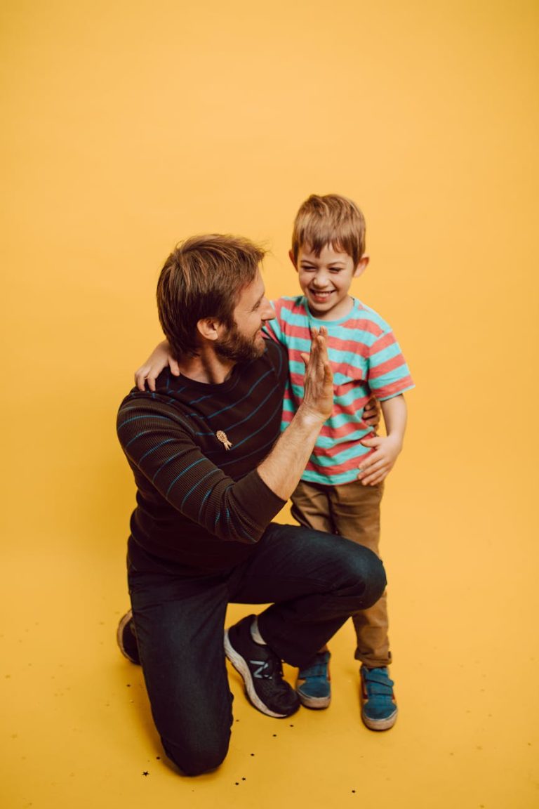 Father and son sharing a joyful high five indoors against a vibrant yellow background.