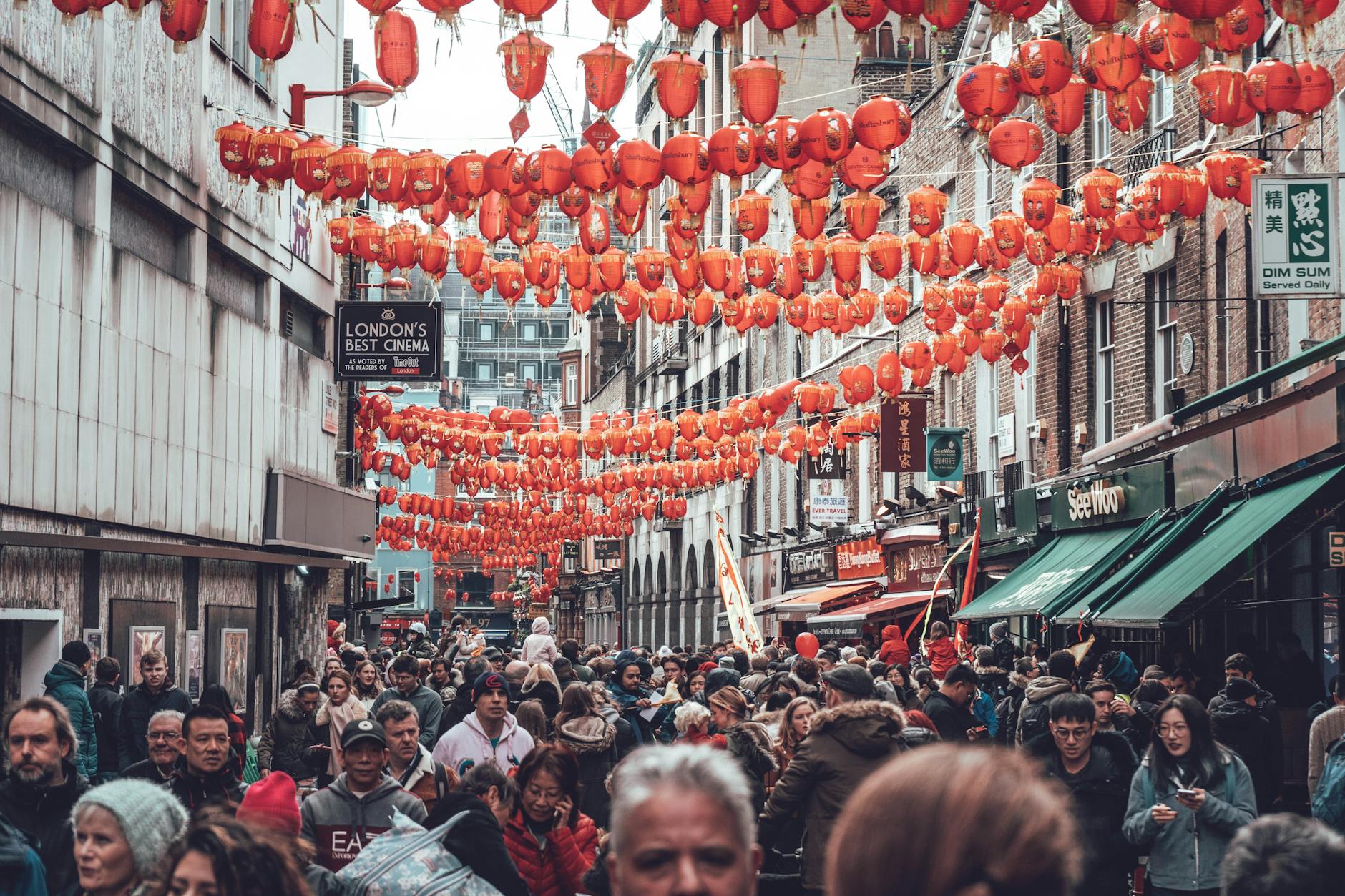 Crowded street in London's Chinatown adorned with traditional red lanterns, capturing vibrant cultural atmosphere.