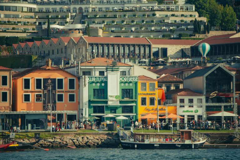 Colorful architecture along the Porto riverside with vibrant facades, lively street, and scenic backdrop.