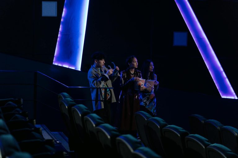 Three friends standing in a dimly lit cinema holding popcorn, enjoying a movie night.