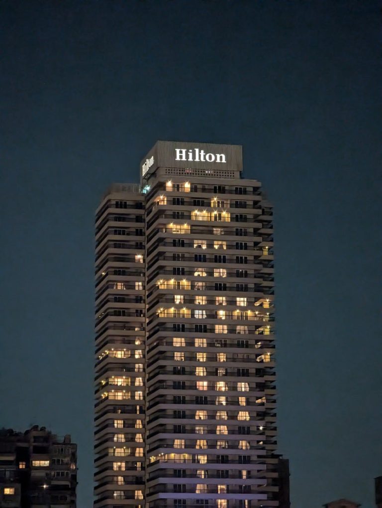 High-rise Hilton hotel building, illuminated at night against a clear sky. Ideal for cityscape and travel themes.