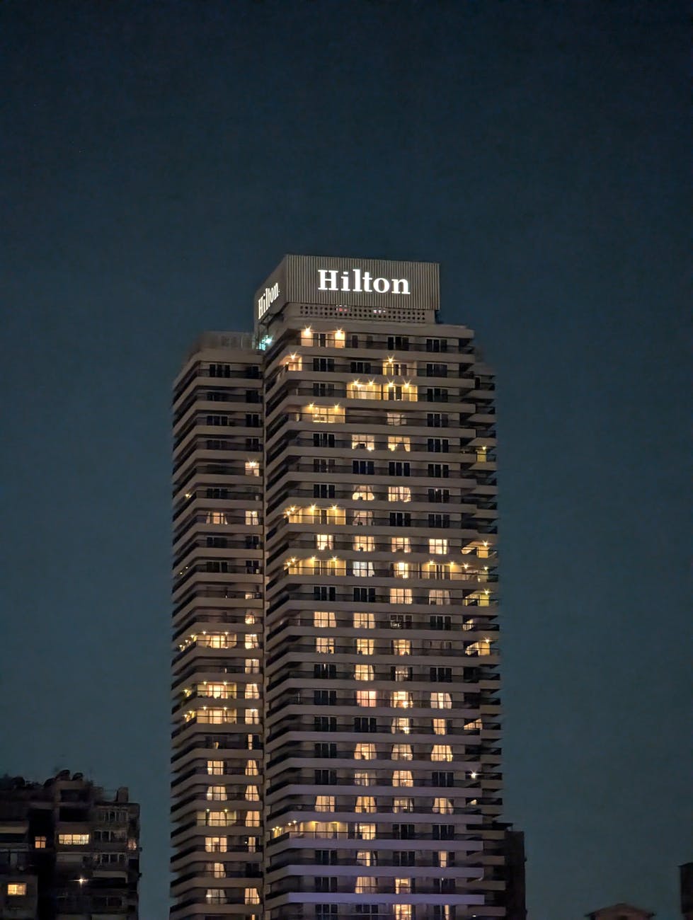 High-rise Hilton hotel building, illuminated at night against a clear sky. Ideal for cityscape and travel themes.
