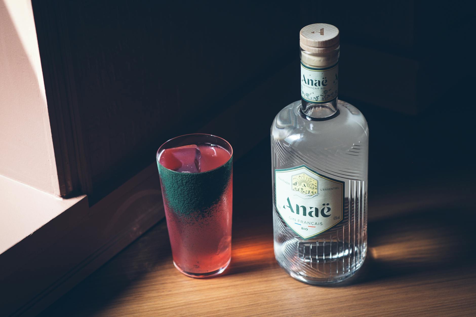 Stylish presentation of Anaë gin bottle beside a refreshing cocktail glass on a wooden surface.