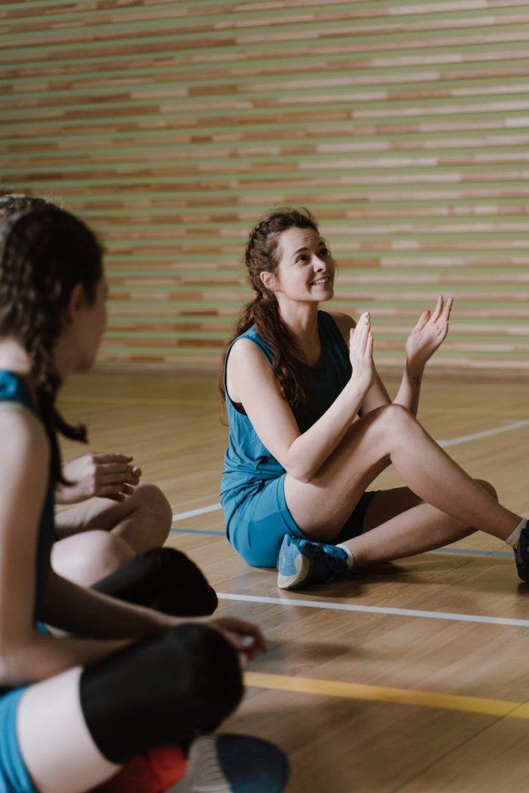 Women athletes in sportswear relax and talk on a basketball court indoors. Perfect for sports and fitness themes.