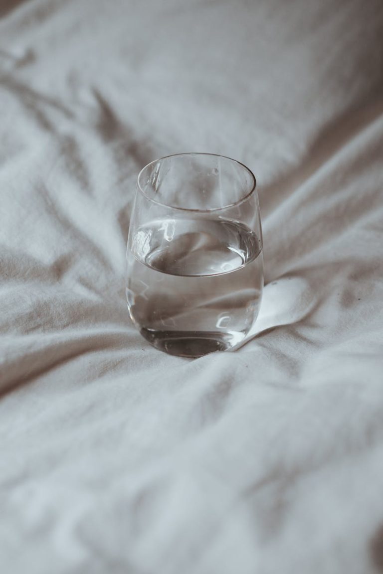 A minimalist photo of a glass of water on a white sheet emphasizing hydration and simplicity.