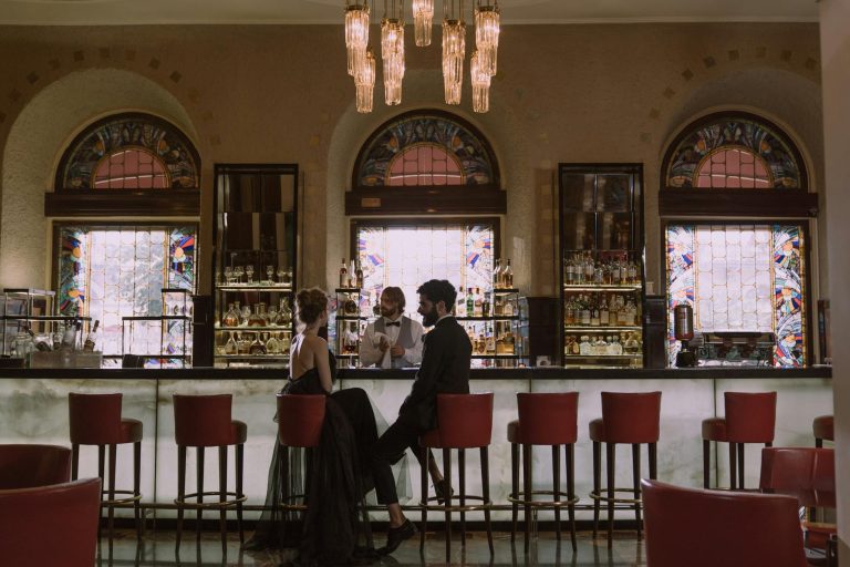 Couple in elegant attire enjoying a date at a luxurious bar with a stained glass backdrop.