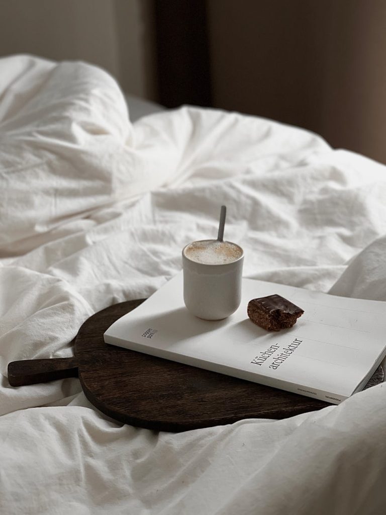 Serene morning scene with a coffee cup, book, and snack on a cozy bed setting.
