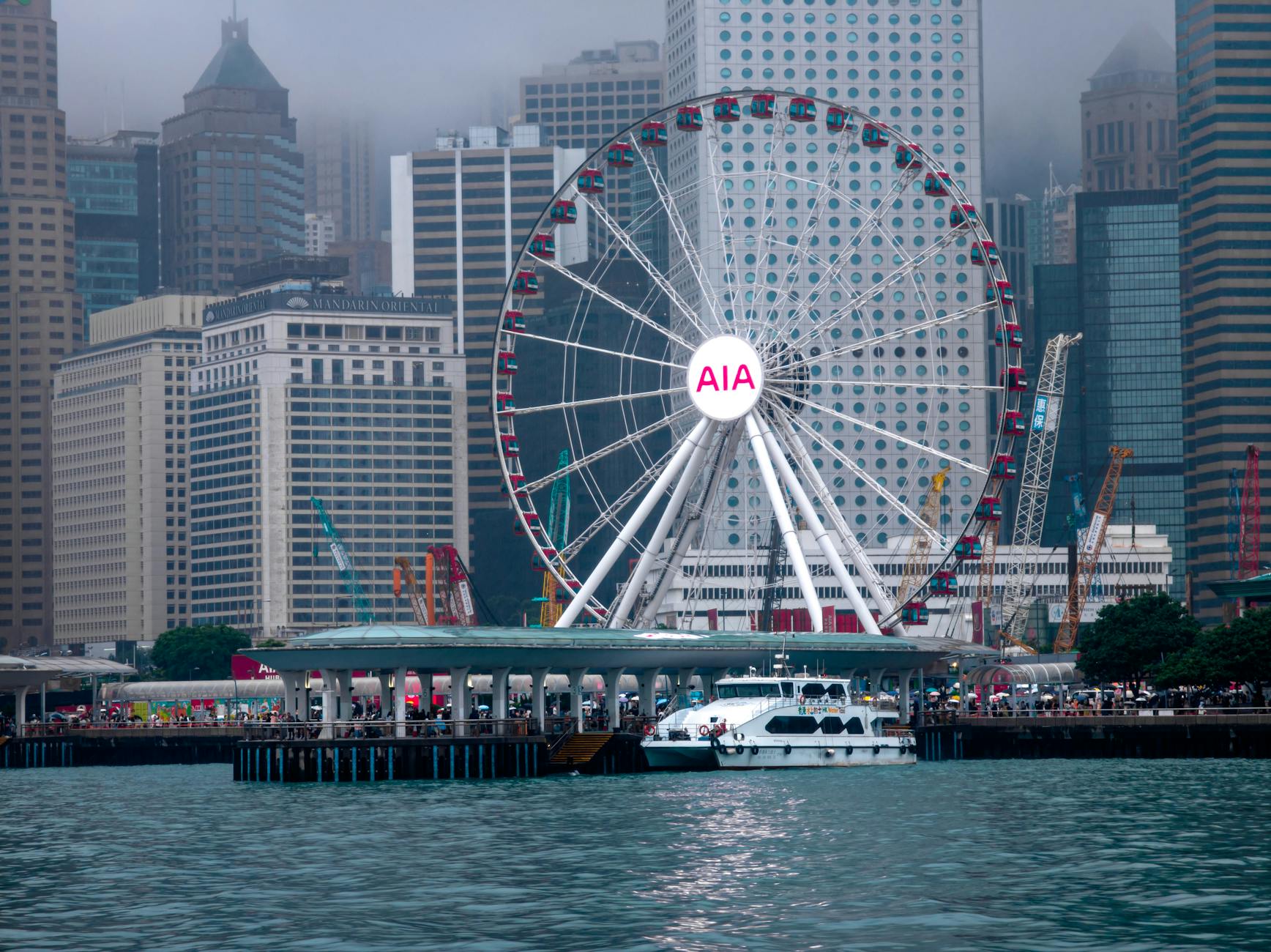 A large ferris wheel by the waterfront against a backdrop of city skyscrapers.