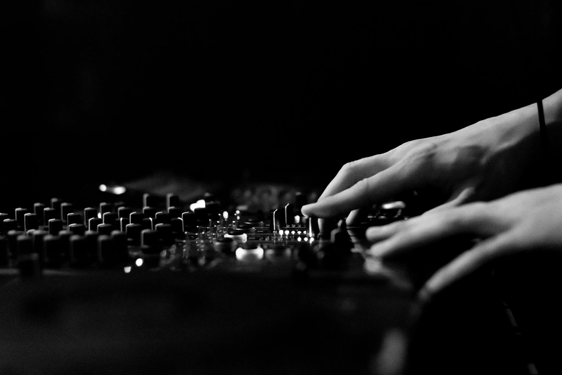 Artistic black and white image of hands adjusting a DJ console in a club.