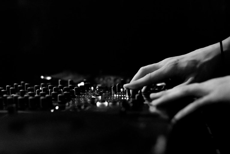Artistic black and white image of hands adjusting a DJ console in a club.