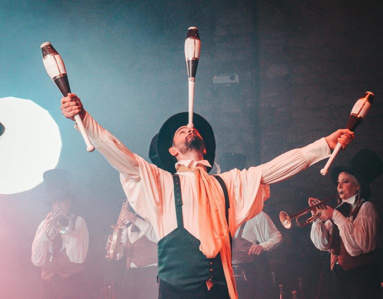 Energetic circus performer juggling clubs in a lively, theatrical setting.