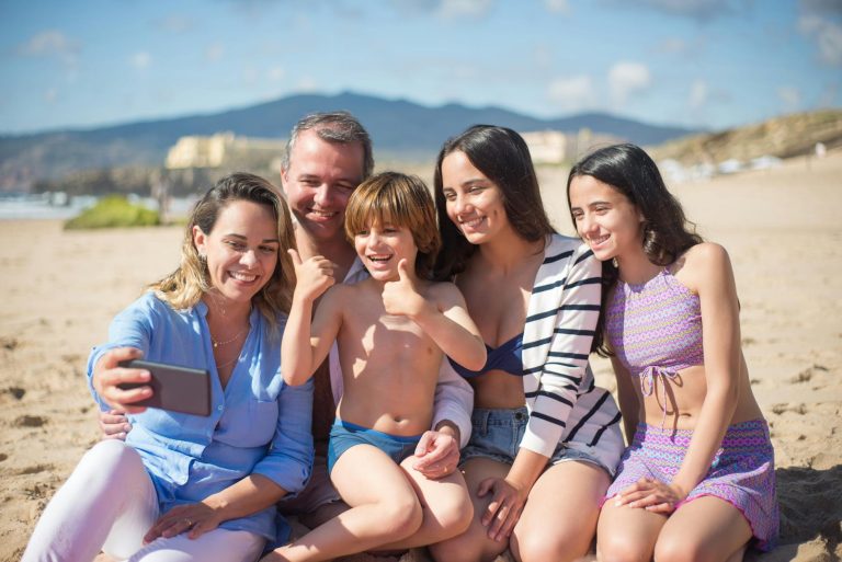Family smiling and taking a selfie on a sunny beach in Portugal.