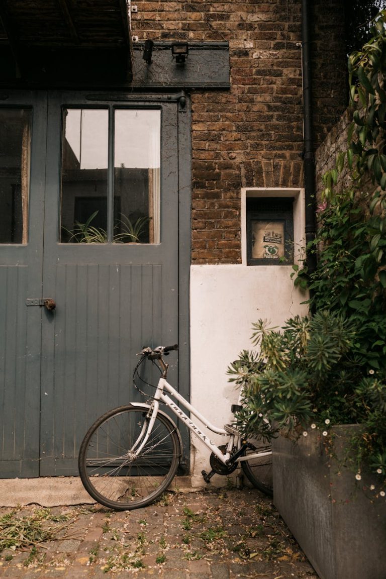 White bicycle parked against rustic red brick wall with grey doors in Notting Hill, London.