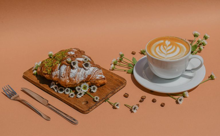 Stylish coffee and croissant setup with flowers and coffee beans on a wooden board.