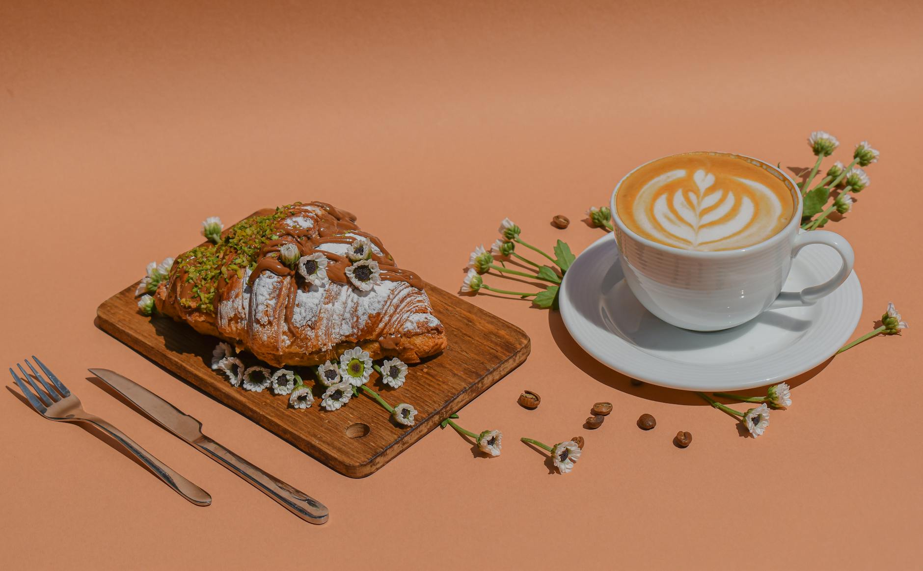 Stylish coffee and croissant setup with flowers and coffee beans on a wooden board.