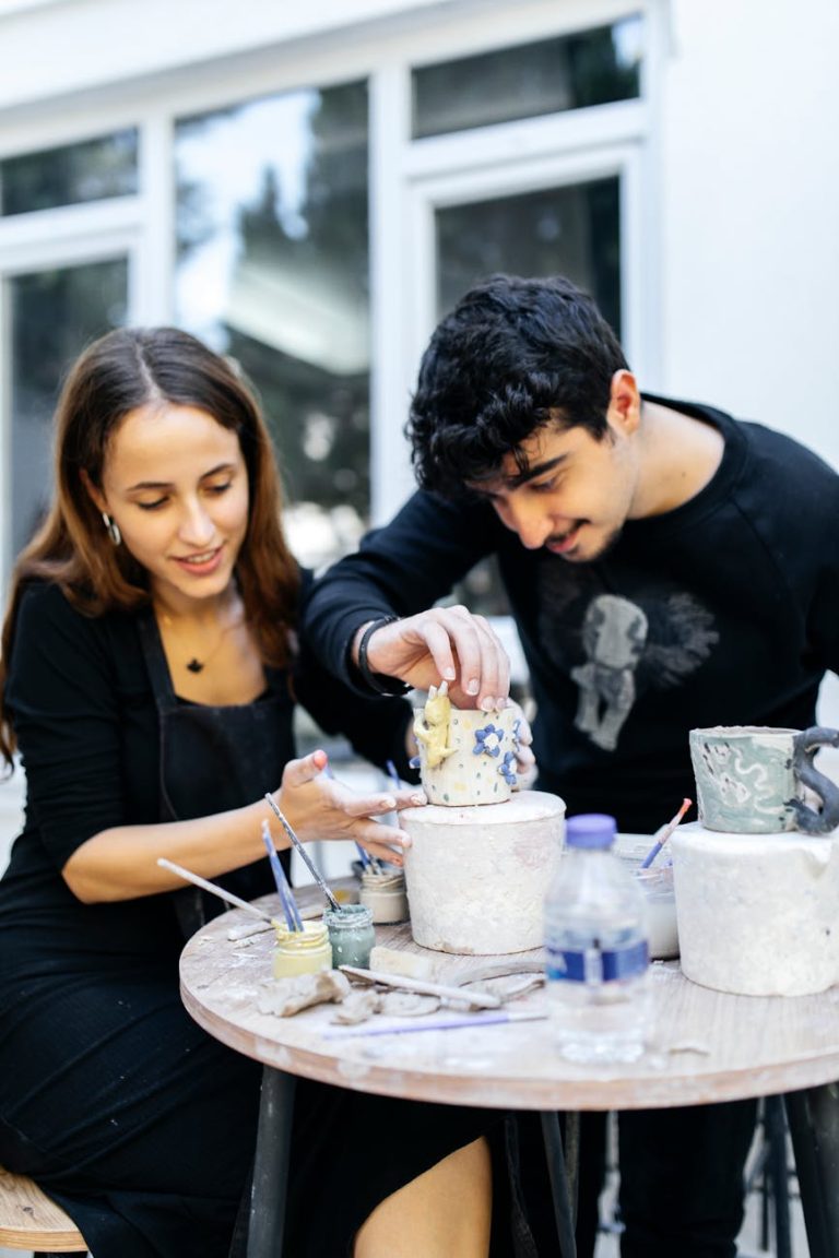A couple enjoying artistic pottery painting together outdoors, showcasing creativity and teamwork.