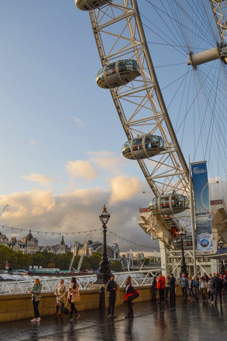 Anonymous people waiting near observation wheel with cables on wet square under cloudy blue sky