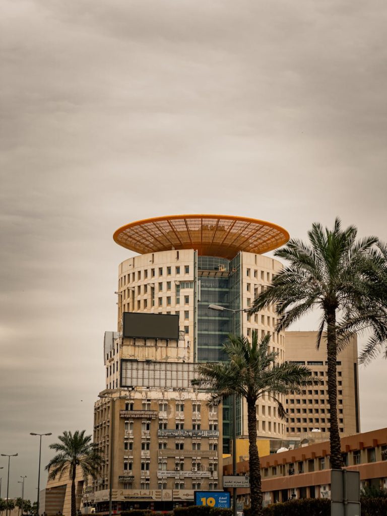 A striking modern building with unique design set against the Kuwait City skyline, featuring palm trees.