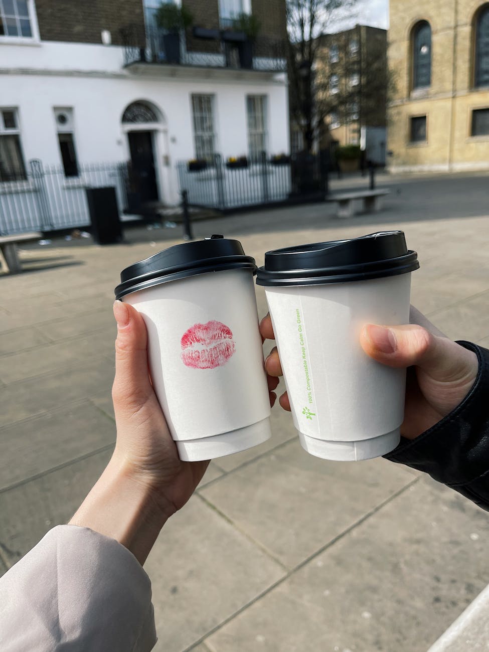 Two people clink takeaway coffee cups on a romantic date in London.