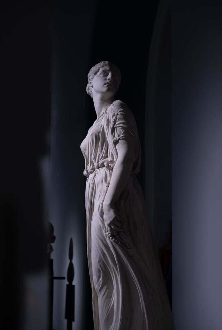 Neo-Classical statue of a Greek goddess with elegant drapery in a shadowy interior.