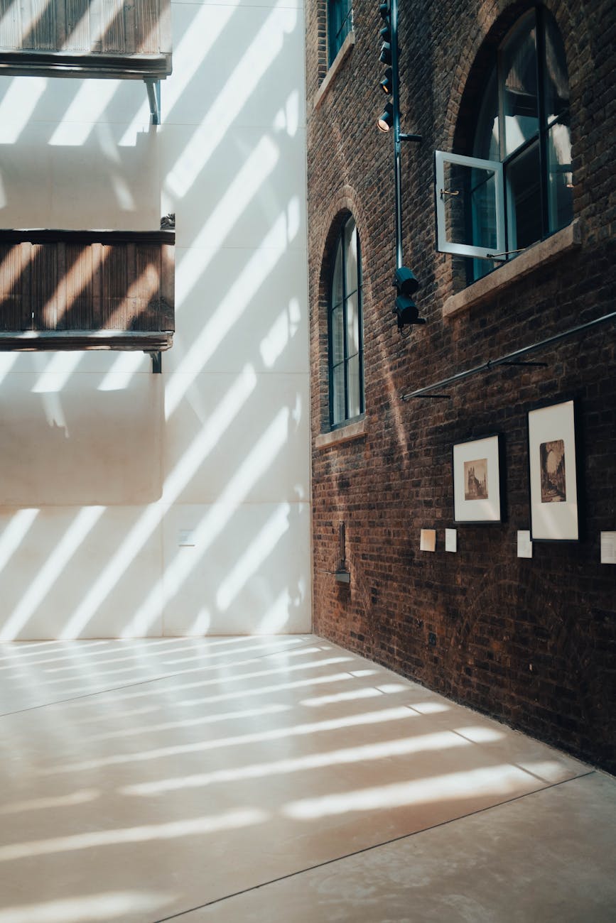 Sunlit museum interior in London with brick walls and artistic shadows creating a dramatic effect.