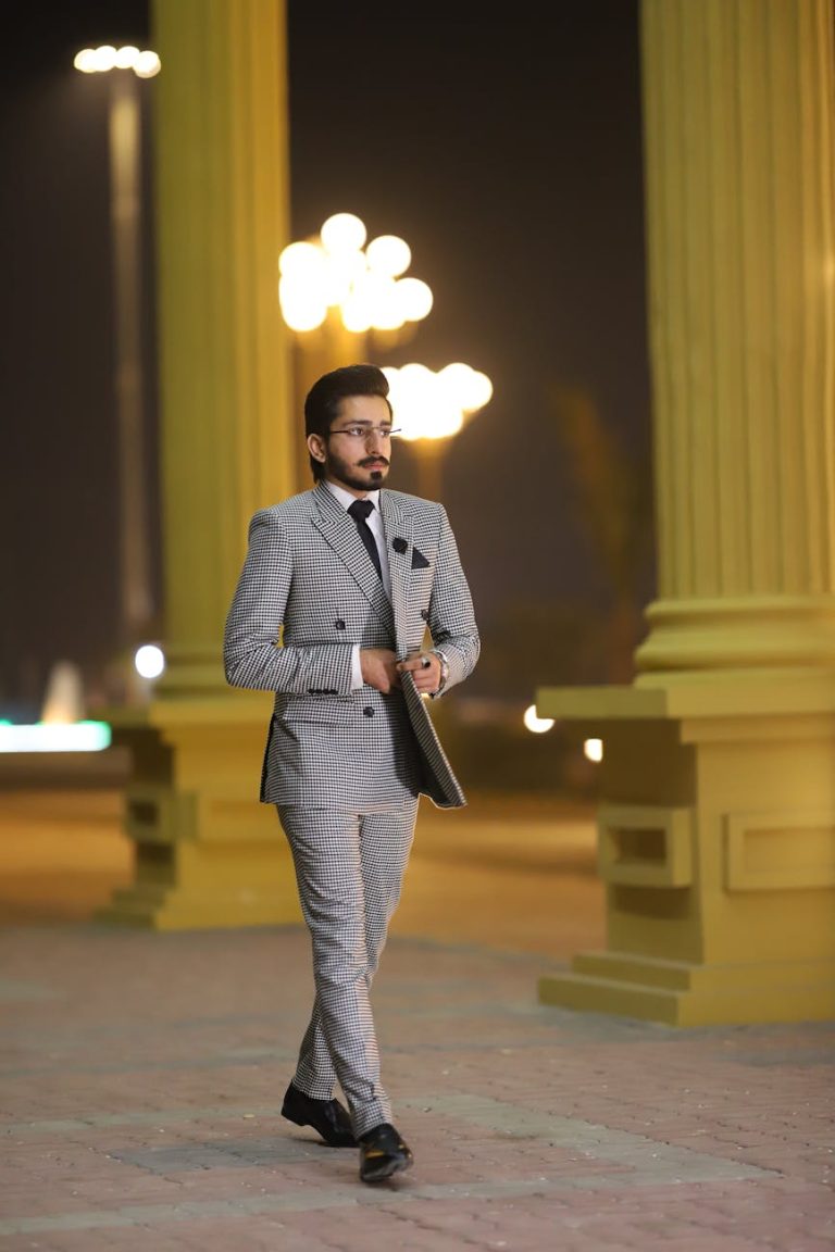 A fashionable man in a checkered suit walking at night in an urban setting.