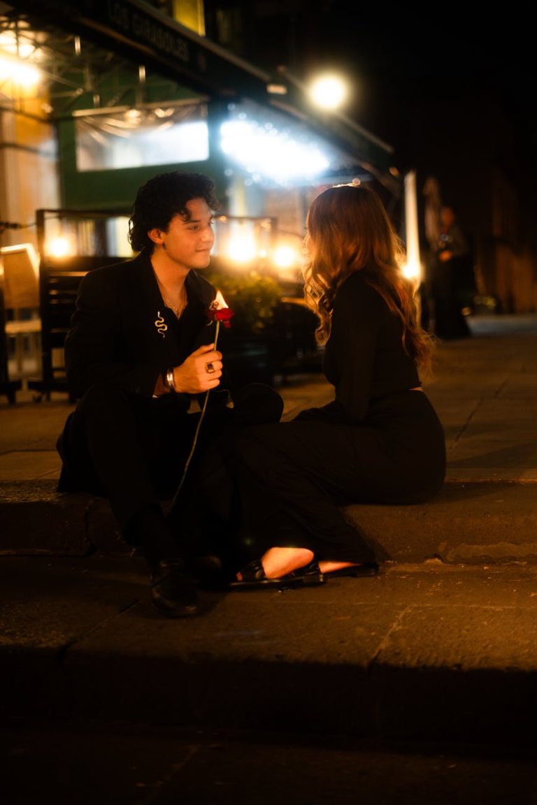 A couple enjoys a romantic evening outdoors with a red rose and warm lighting.