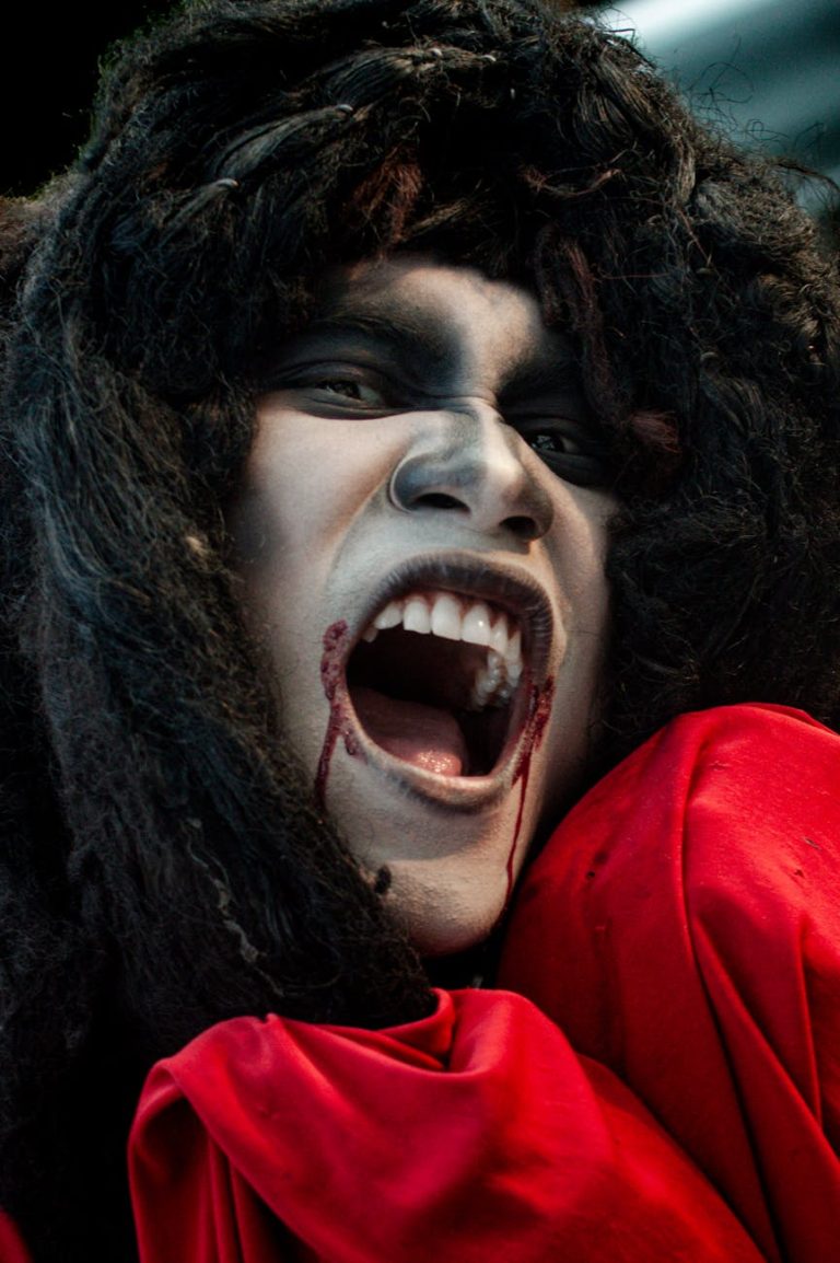 Close-up of a person in dramatic cosplay with face paint and red cloak, expressing emotion.