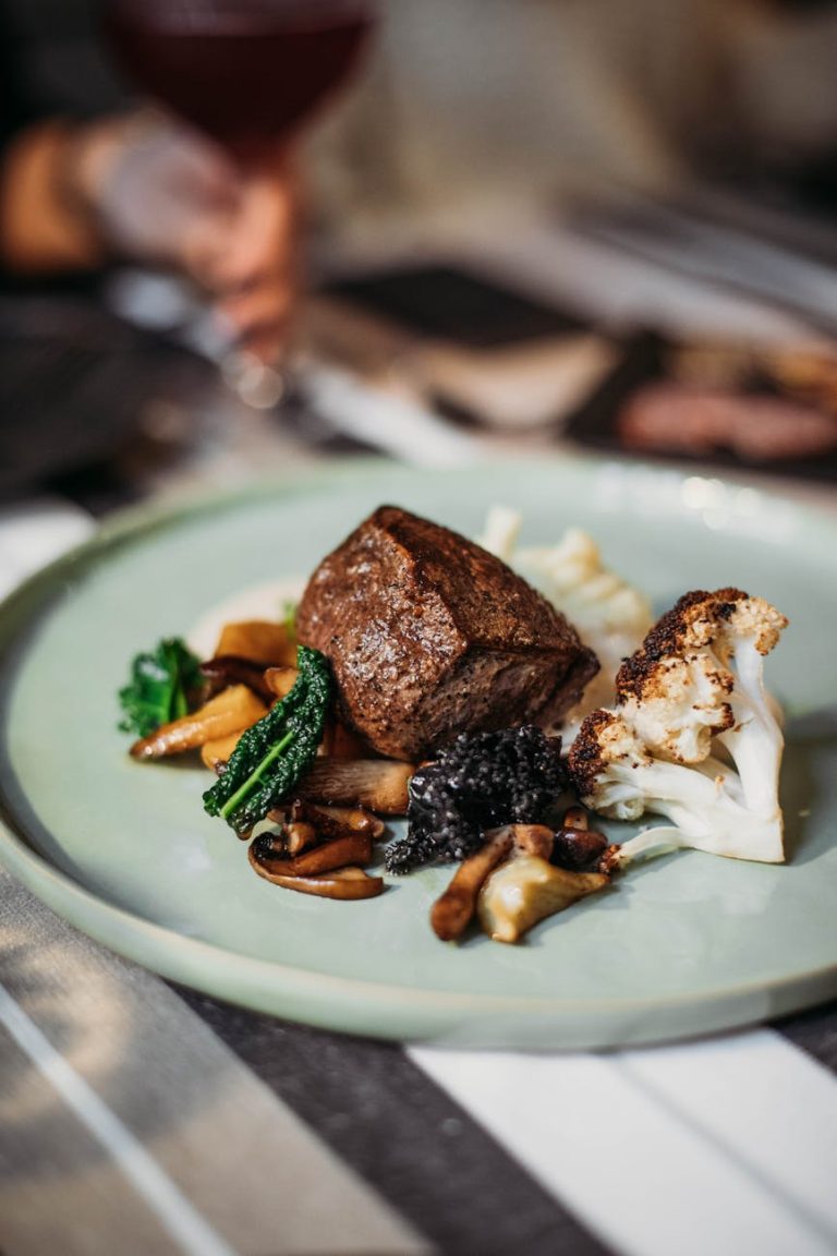 Tasty steak served on plate with white cauliflower and fried mushrooms placed on table in light modern restaurant on blurred background