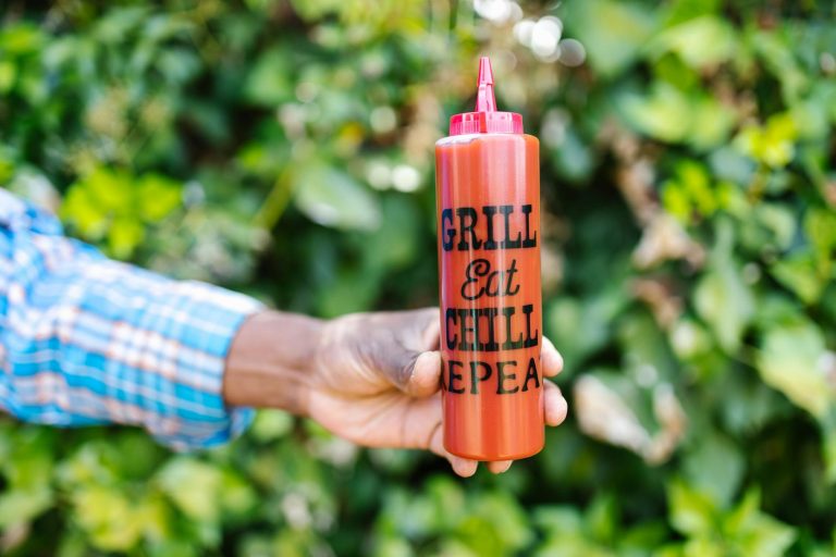 Close-up of a hand holding a ketchup squeeze bottle with text outdoors.