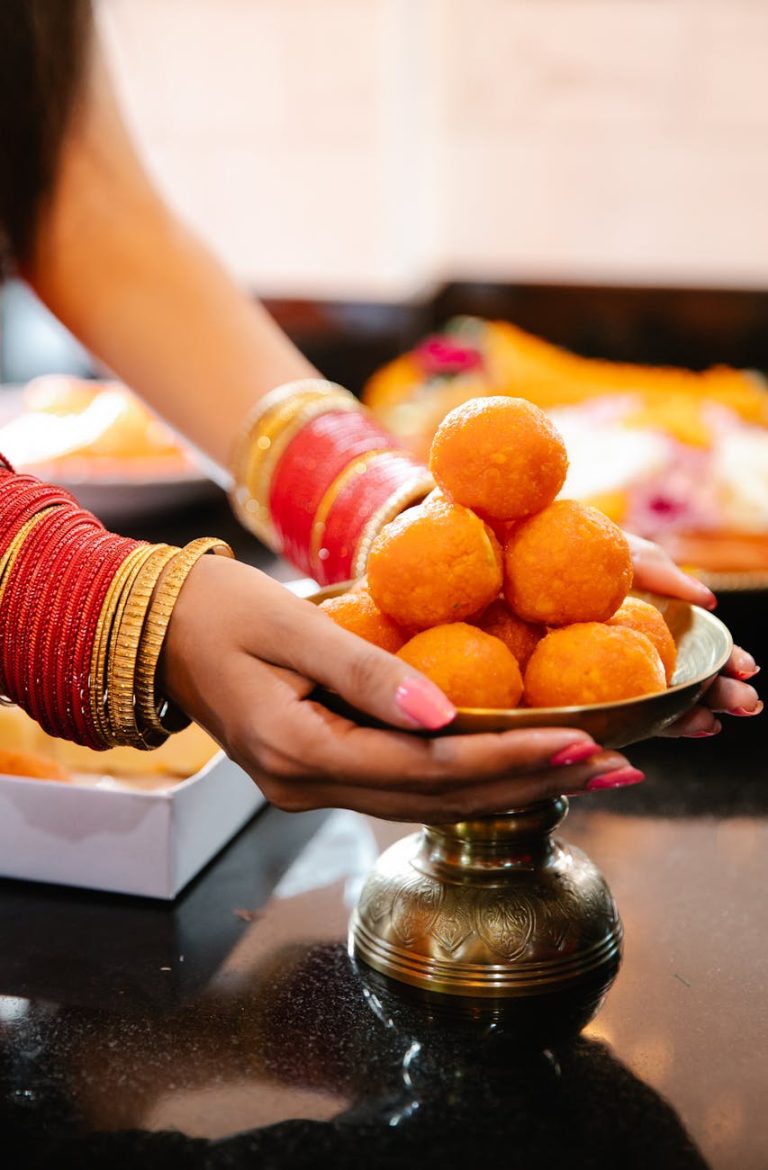 Woman presenting Indian sweets on a brass plate, showcasing cultural celebration.